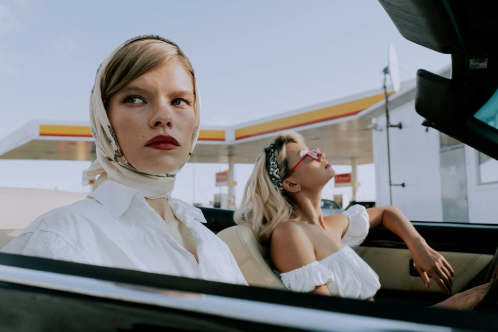 Stylish women in a convertible at a gas station, embracing classic fashion.