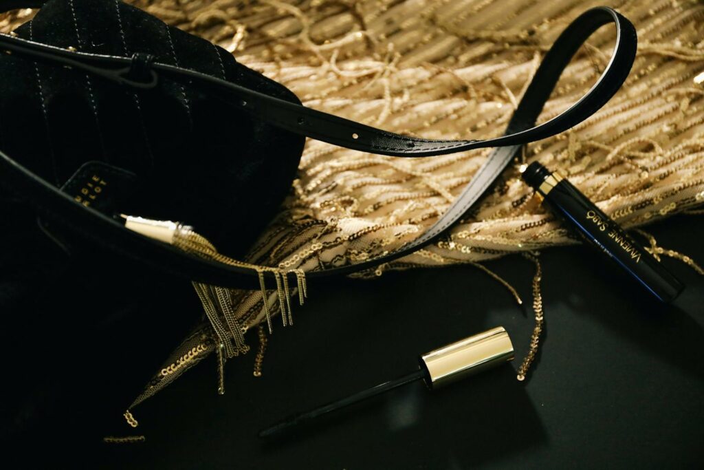 Close-up of a black handbag and mascara on a gold sequined fabric, capturing luxury fashion essence.