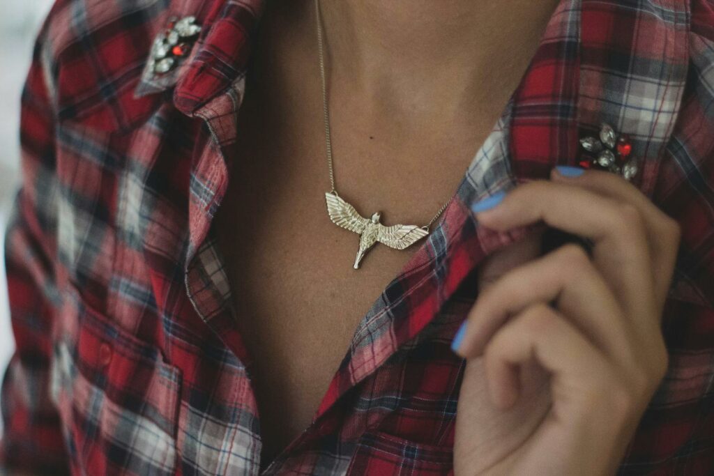 Fashionable woman in plaid shirt with a bird necklace, showcasing style.