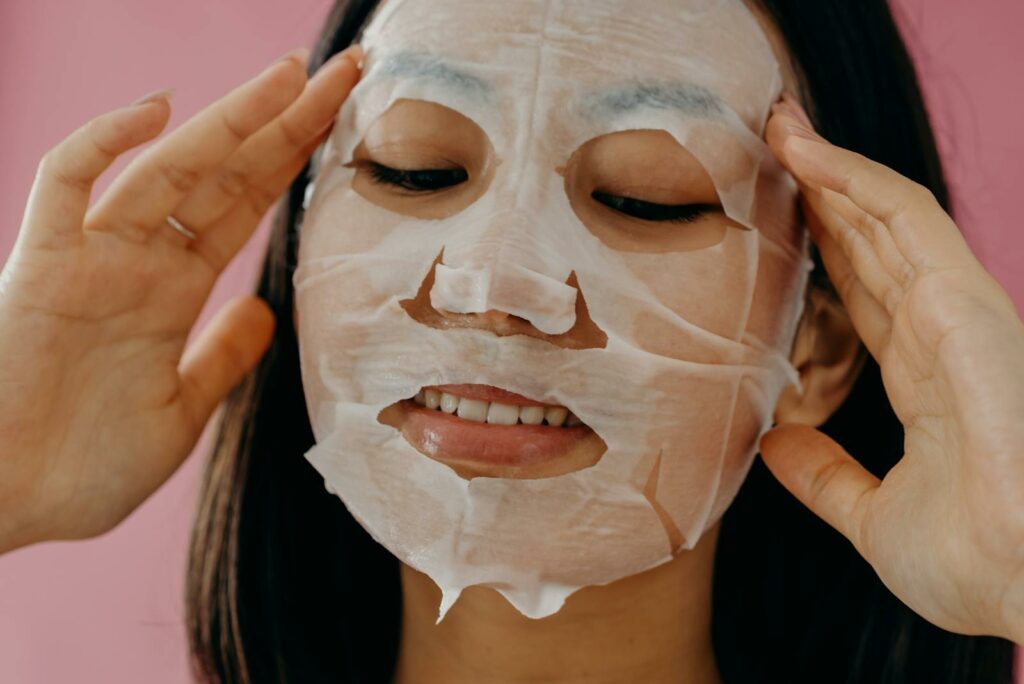 Close-up of an Asian woman applying a hydrating sheet mask for skincare routine.