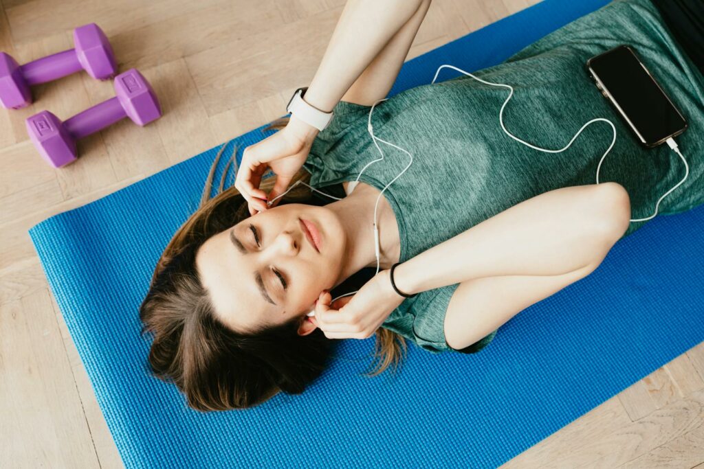 Young woman enjoying music while relaxing on a yoga mat indoors, embodying tranquility and mindfulness.