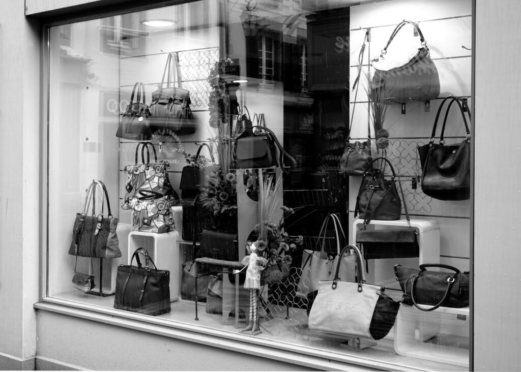 Black and white photo of a boutique window showcasing luxury handbags on display.